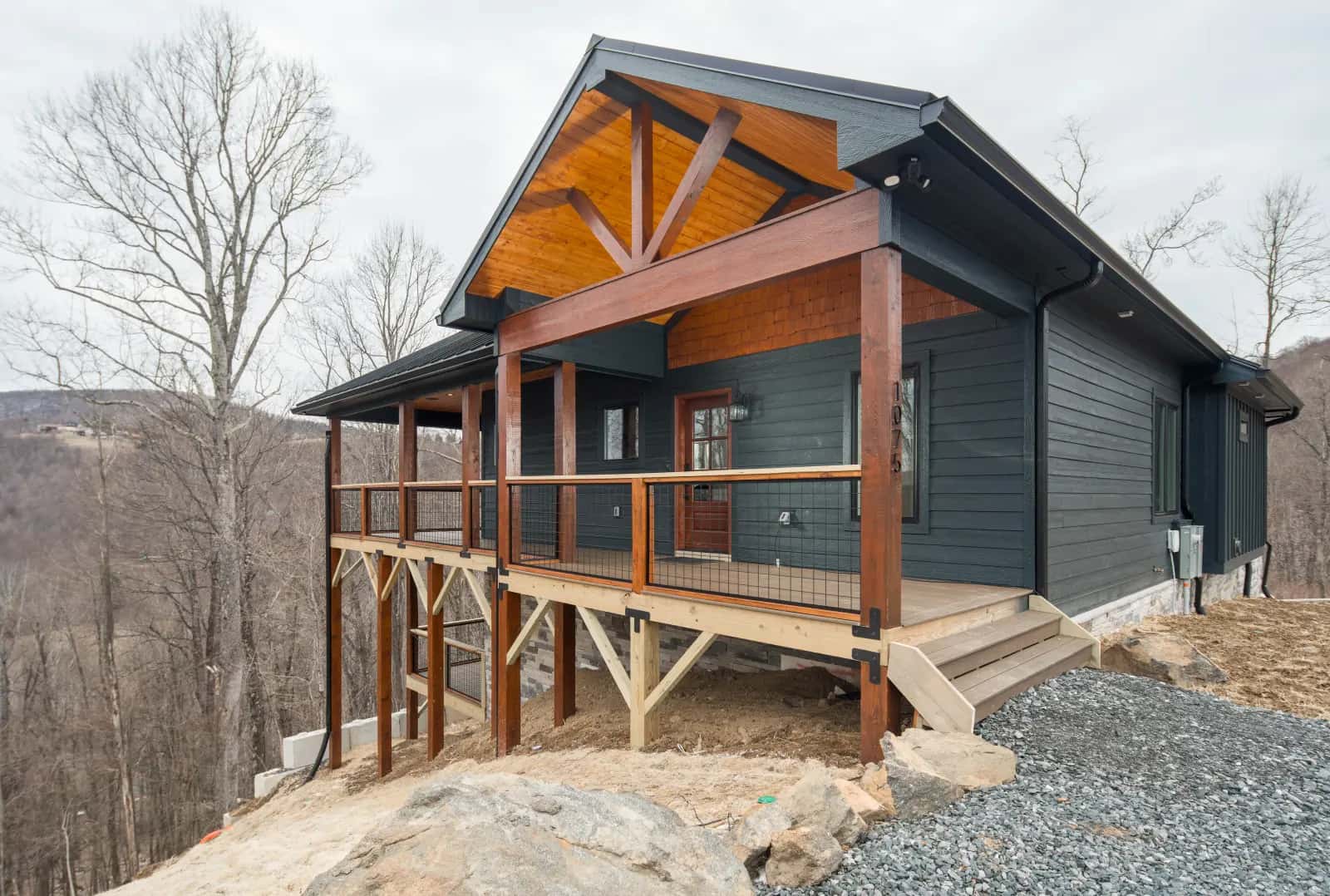 Custom mountain home with dark siding, a metal roof, and a timber-framed deck on a hillside in Ashe County, NC